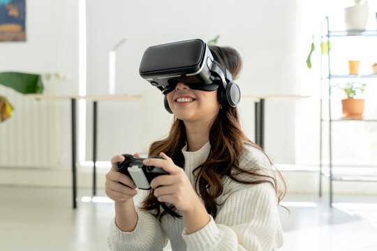 Smiling woman with game controller using virtual reality headset at home