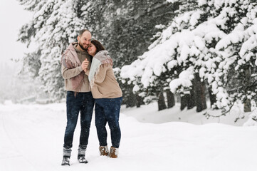 Fototapeta na wymiar Walk in winter. Embracing couple enjoying snowfall. Man and woman having fun in the frosty forest. Romantic date in winter time.Christmas mood of a young family. Love and leisure concept
