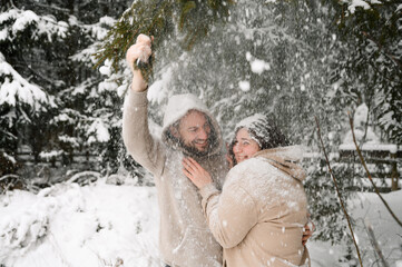 Walk in winter. Embracing couple enjoying snowfall. Man and woman playing with snow in the frosty forest. Romantic date in winter time.Christmas mood of a young family