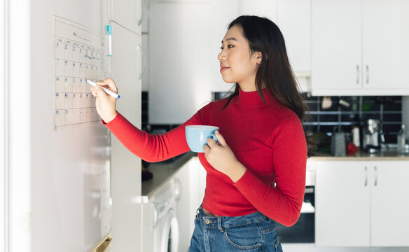 Young woman writing on calendar in kitchen