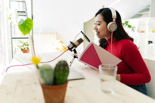 Smiling woman with book podcasting at home