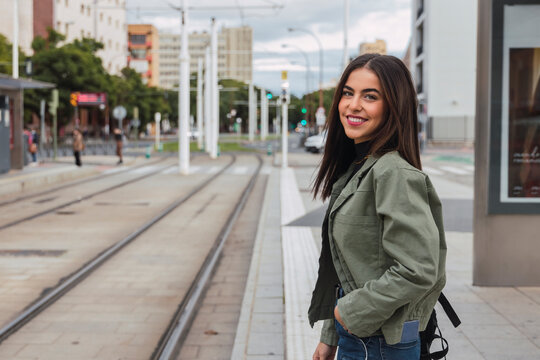 Smiling woman with hand in pocket at tram station