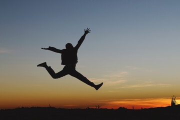 Silhouette of happy girl jumping playing on mountain at sunset or sunrise