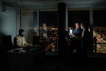 Group of young intercultural co-workers computing in large openspace office at night