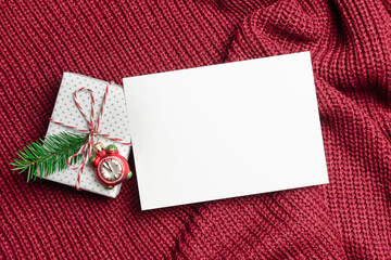 Christmas or New Year greeting card mockup with decorated gift box on red knitted background