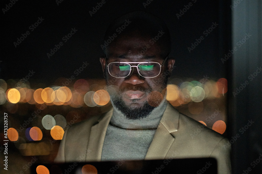 Aufkleber serious african businessman in eyeglasses looking at computer screen while working late in the night