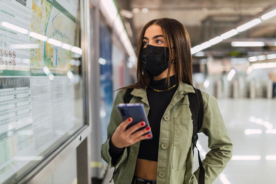 Woman with face mask and mobile phone checking map in subway