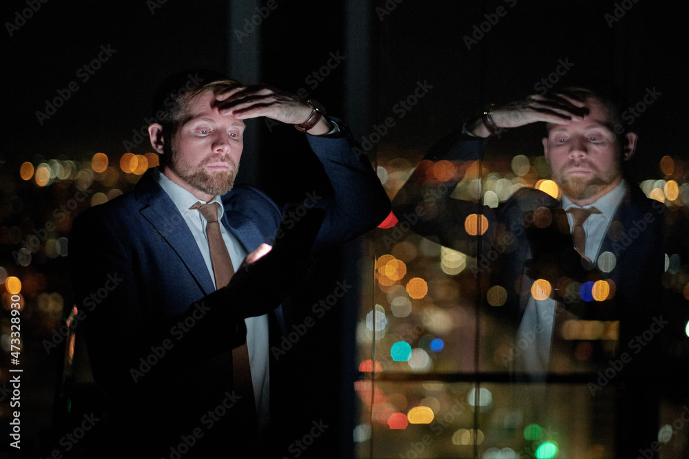 Poster young contemporary businessman scrolling in smartphone by large window while staying in office at ni