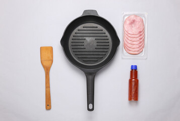 Fototapeta na wymiar Frying pan with ham, ketchup and a spatula on a gray background. Top view