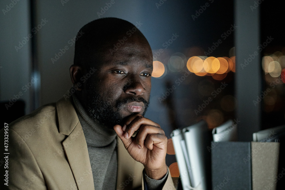 Poster serious man in formalwear sitting in front of computer monitor and looking through data on screen wh