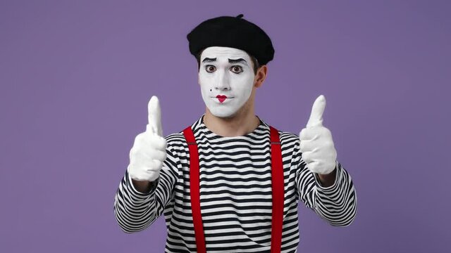 Excited cheerful stunning marvelous happy young mime man with white face mask wears striped shirt beret showing thumb up like gesture isolated on plain pastel light violet background studio portrait