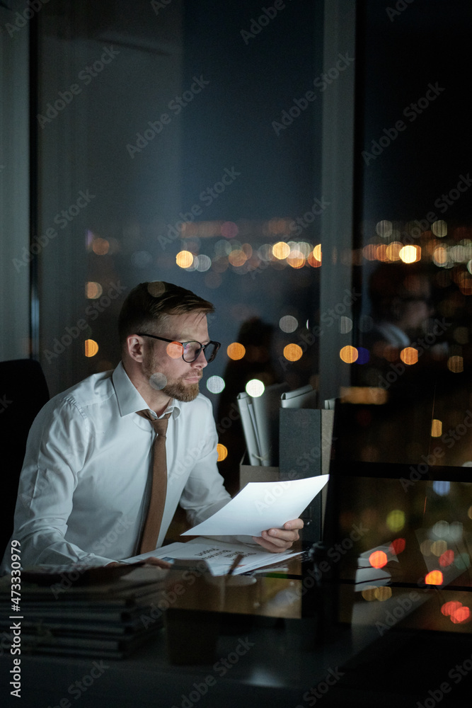 Poster Young economist with paper networking in front of computer late at night in openspace office