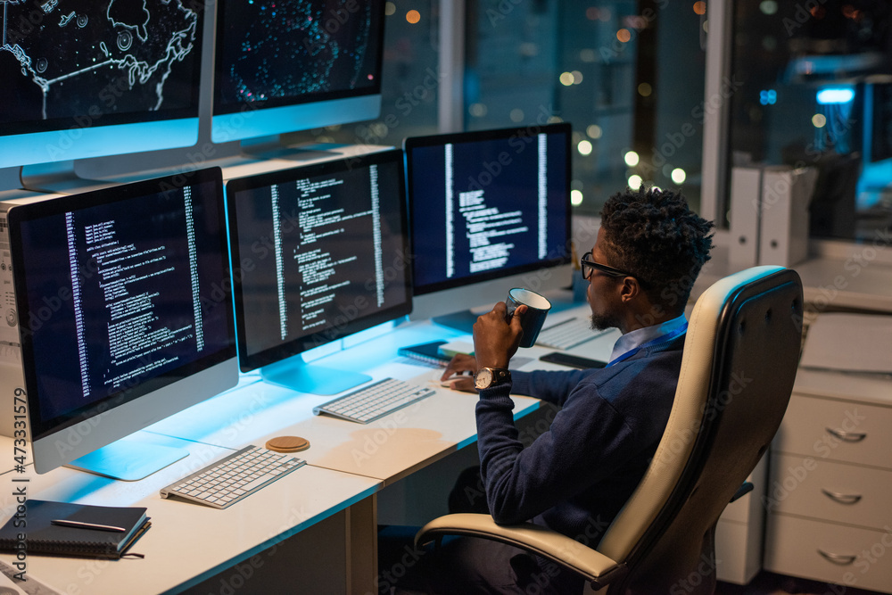 Aufkleber Young African programmer with drink looking at coded data on computer screen while working in office