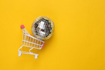 Shopping cart with disco ball on yellow background. Party concept. Creative minimal layout. Top view