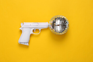 Gun with disco ball on yellow background. Party concept. Creative minimal layout. Top view