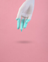 Plastic hand with dripping turquoise paint on a pink background. Minimal creative layout. Concept art