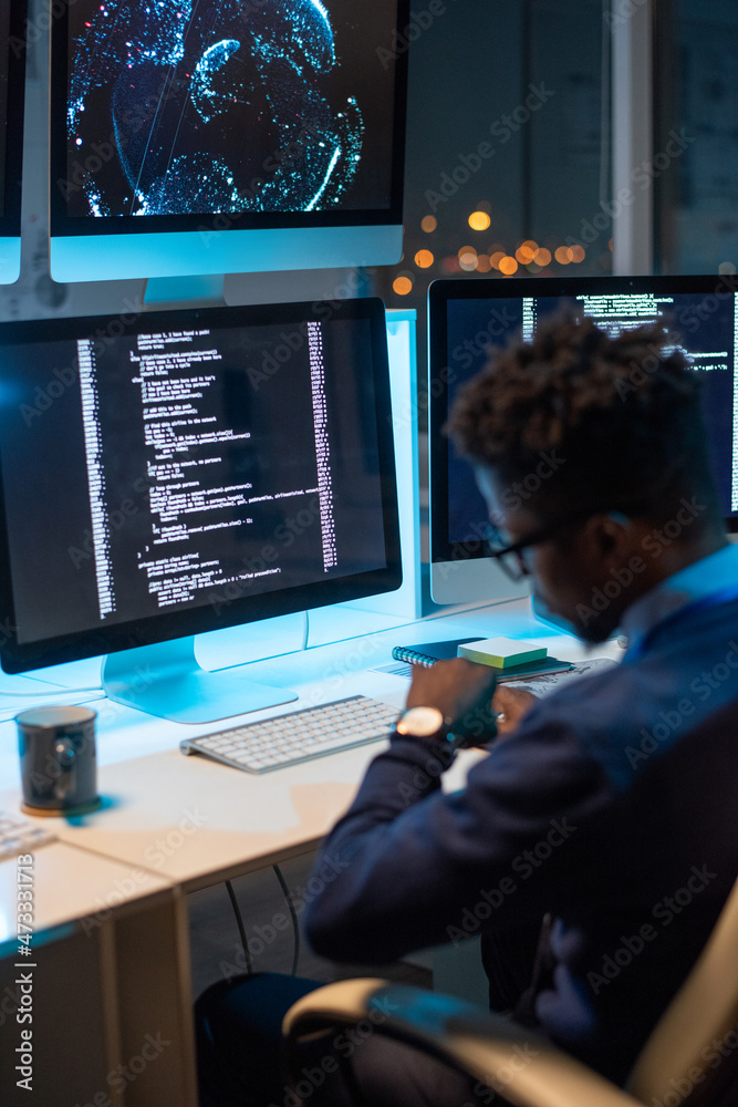 Poster busy young programmer of african ethnicity looking at wristwatch while working late in the evening i