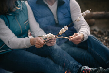 Couple fries marshmallows on sticks by the fire. Blurred, selective focus on marshmallows.