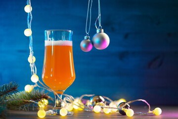 A glass of festive Christmas beer ale on a wooden blue background. Christmas tree branches and a...