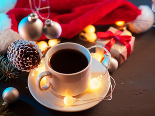 A white cup of espresso coffee on a festive table with gifts, a yellow round garland, a Santa Claus hat and a bump