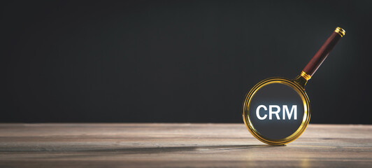 Magnifying glass with text CRM on wooden table.