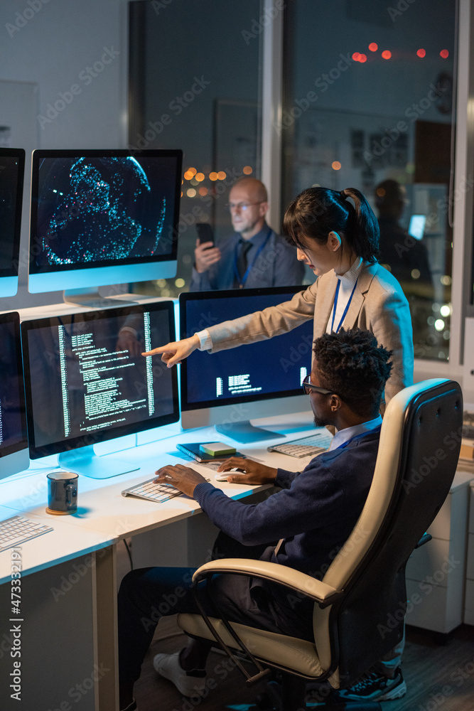 Poster Young Asian businesswoman pointing at computer screen with decoded data while discussing it with African male colleague