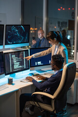 Young Asian businesswoman pointing at computer screen with decoded data while discussing it with African male colleague