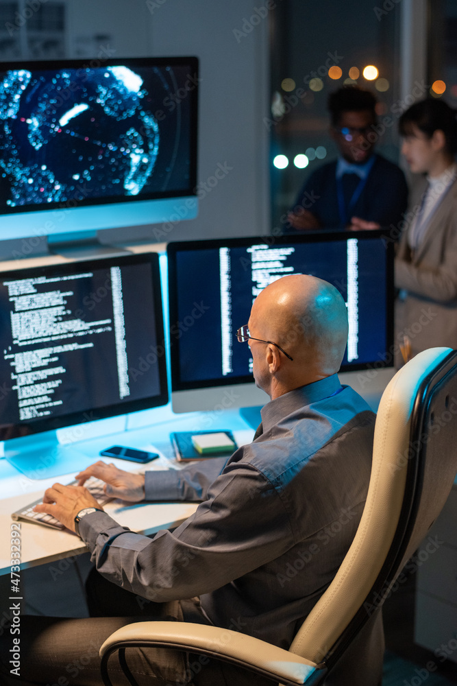 Aufkleber Bald mature businessman decoding data on computer screen while working overtime in office