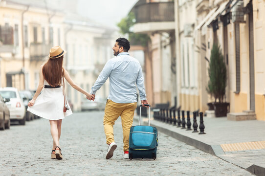 Joint, romantic trip. Loving international couple of tourists with travel luggage are walking along a European street. Spend time together.