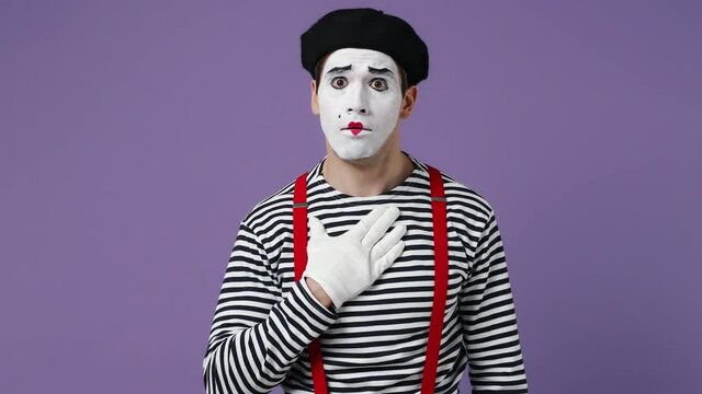 Charismatic young mime man with white face mask wears striped shirt beret look camera listen intently nodding rely on invisible thing isolated on plain pastel light violet background studio portrait