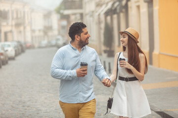 Fototapeta premium International couple in love drinking coffee walking around the city, holding hand