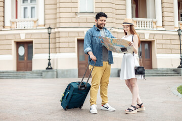 International couple of tourists walking along a European street with travel luggage and studying city map
