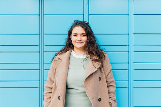 Smiling curvy woman wearing overcoat in front of blue wall