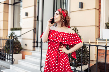 Young beautiful woman in red polka dot dress talking on phone outdoors