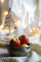 Bowl of apples and soft blanket with lit candles and Christmas decorations in the background. Selective focus.