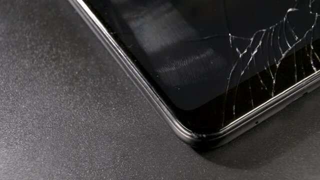 Broken smart phone rotates by with cracked screen in close up macro view.  Smashed screen on touchscreen, e-waste concept.