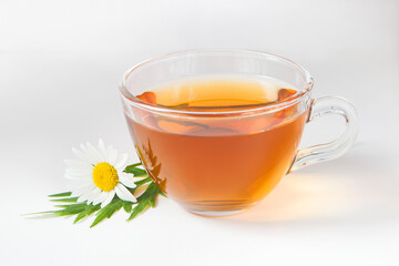 Transparent glass cup with chamomile tea on a white background. A daisy flower lies next to the cup.