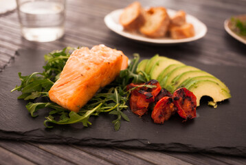 Baked sea trout fillet with fresh vegetables and herbs on black board