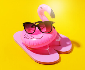 Inflatable pink flamingo with sunglasses, flip flops on yellow sunny background. Summer, beach vacation concept. Minimalism.