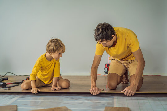 Father and son installing new wooden laminate flooring on a warm film floor. Infrared floor heating system under laminate floor
