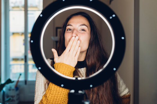 Influencer blowing kiss standing in front of illuminated ring light