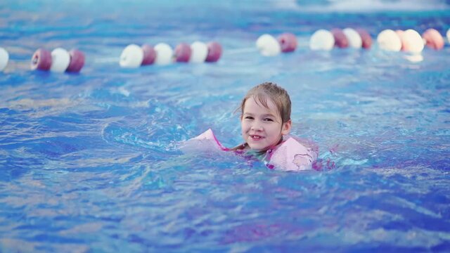 a funny little girl swims in inflatable armbands in a pool