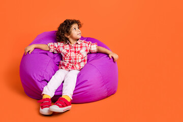 Full length photo of funny small brunette girl sit look wear shirt pants shoes isolated on orange color background