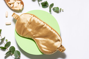 Sleeping mask and natural herbal pills on white background with fresh green eucalyptus twigs....
