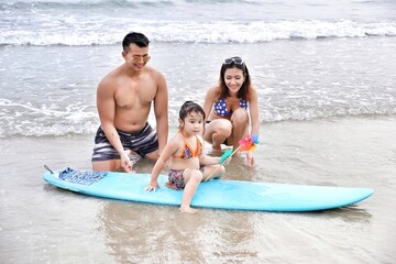 asia family father and mother and daughter happy life on the beach with surfboard, travel the sea in rayong thailand