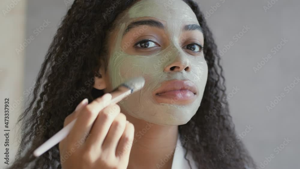 Wall mural Home beauty procedures. Mirror pov of young african american woman applying pampering natural clay mask on her face