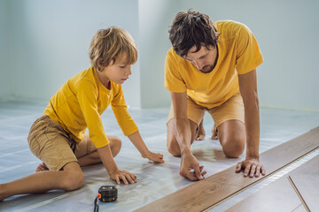 Father and son installing new wooden laminate flooring on a warm film floor. Infrared floor heating...