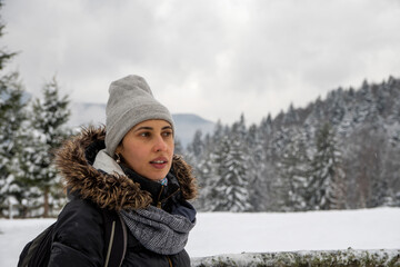 Young woman backpacker in winter forest enjoying snowy mountains. Woman Traveler with backpack hiking. Snow forest on background. Active people concept.