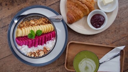 Top view of the table with vegan healthy breakfast: fruit oat vitamin bowl, vegan croissant with organic jam and dairy-free butter, matcha latte 