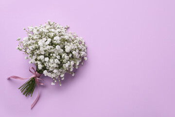 Bouquet of white gypsophila with ribbon on violet background, top view. Space for text